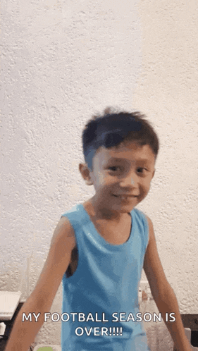 a young boy in a blue tank top is smiling while standing in front of a wall .