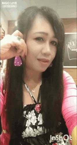 a woman is wearing a pink sweater and purple earrings while taking a selfie .