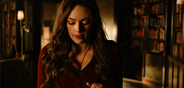 a woman in a red sweater is standing in a dark room looking down .
