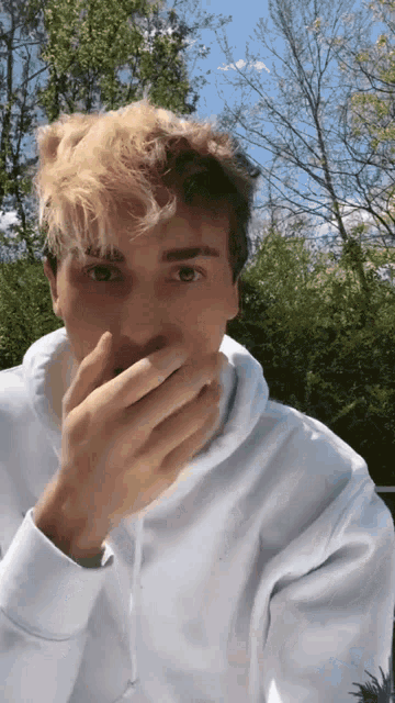 a young man in a white hoodie covering his mouth with his hands