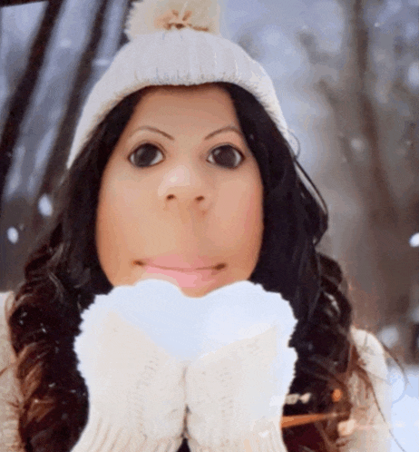 a woman wearing a white hat and gloves is holding a snowball in her hands
