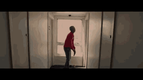 a man in a red shirt is standing in a hallway looking out of a window .