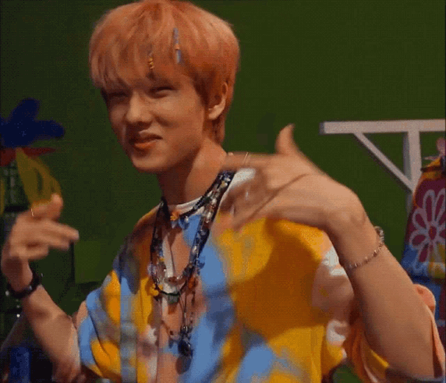 a young man with pink hair is making a peace sign with his hands while wearing a colorful shirt .
