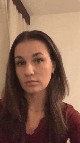 a woman in a red shirt is making a funny face while standing in front of a white curtain .