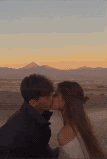 a man and a woman are kissing in front of a mountain
