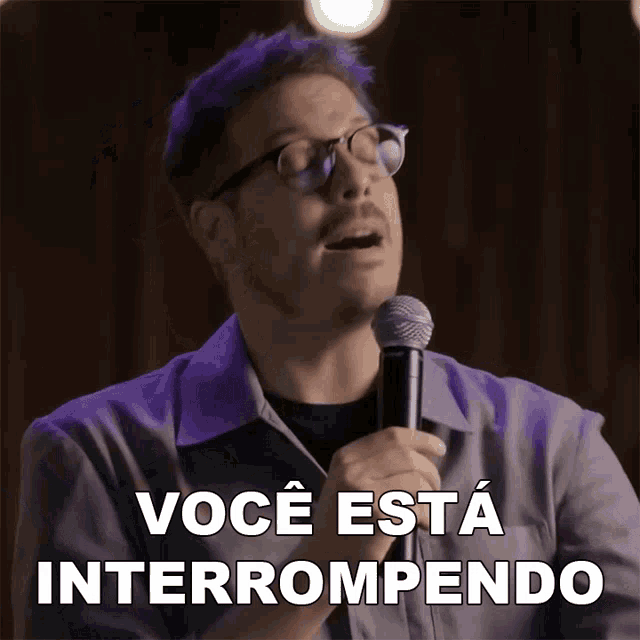 a man with glasses is holding a microphone and says " você esta interrompondo "