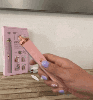 a woman with purple nails is holding a pink device on a wooden table .