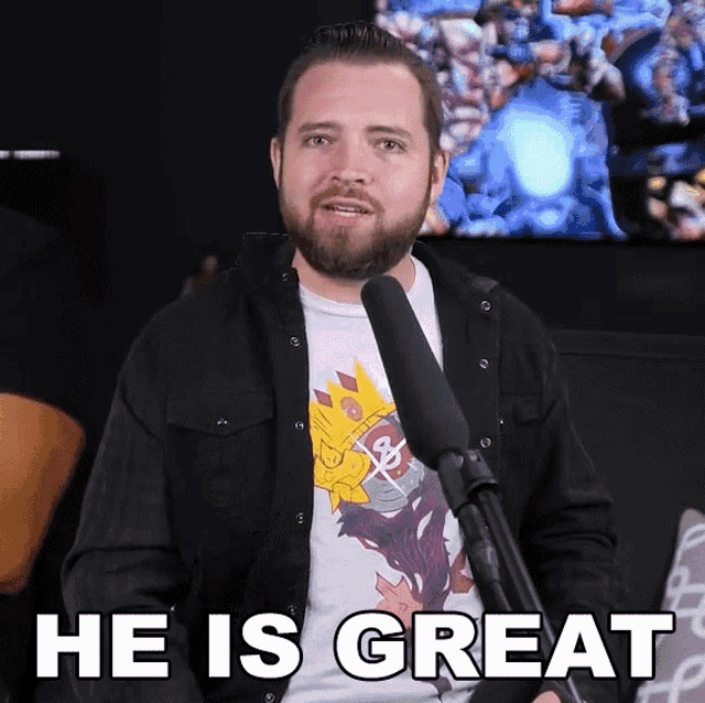 a man with a beard stands in front of a microphone and says " he is great "