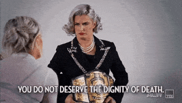 a woman in a suit and pearls is holding a wrestling belt and talking to another woman .