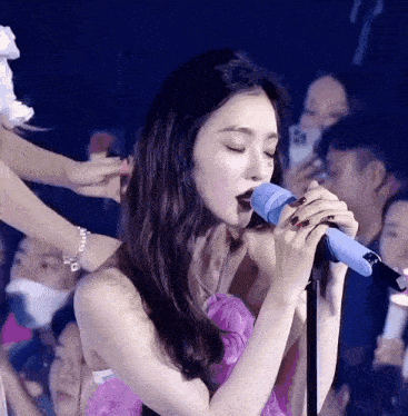 a woman is singing into a microphone in front of a crowd .