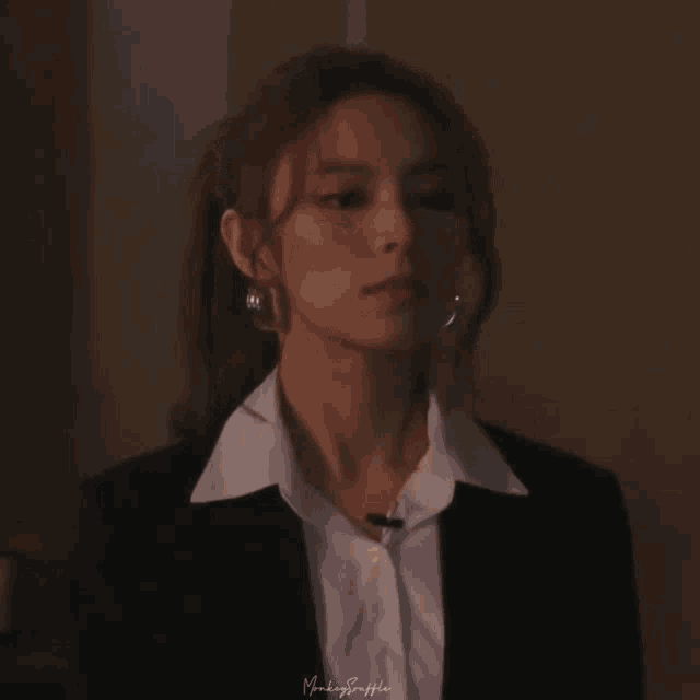 a close up of a woman wearing a suit and white shirt with a ponytail