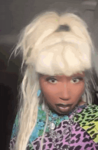 a woman with blonde hair and black skin is wearing a leopard print shirt and a wig .