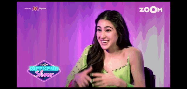 a woman in a green top is sitting in front of a purple background .