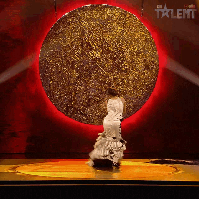 a woman in a white dress is dancing in front of a large gold circle that says got talent on the bottom