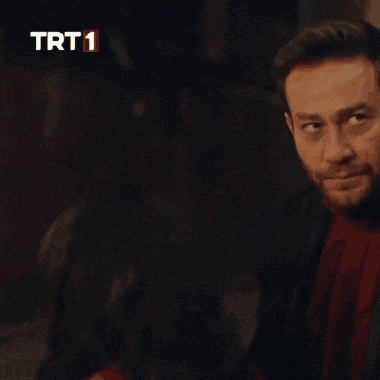 a man with a beard is talking to another man in front of a trt 1 sign