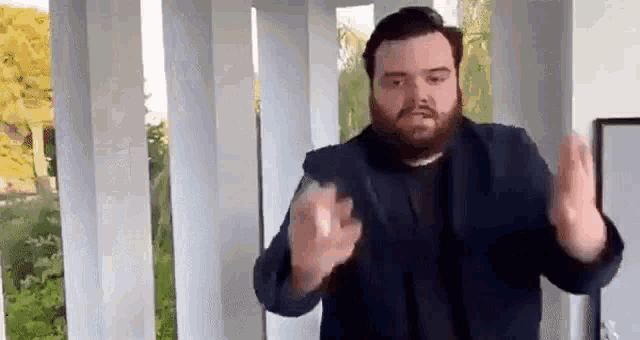 a man with a beard is standing in front of a balcony with his hands in the air .