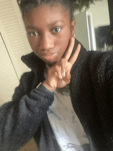 a young girl wearing a black jacket and a white shirt giving a peace sign
