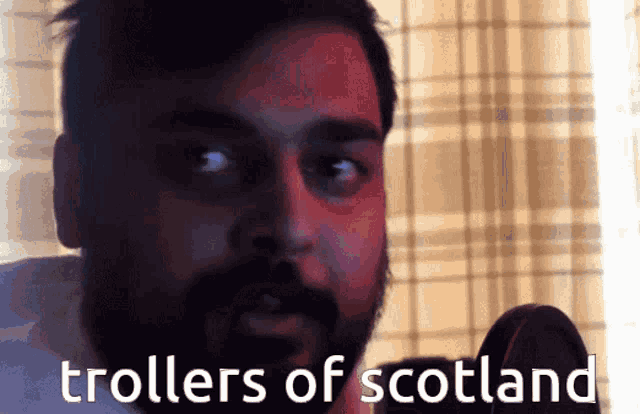 a man with a beard is talking into a microphone with the words " trollers of scotland " written below him