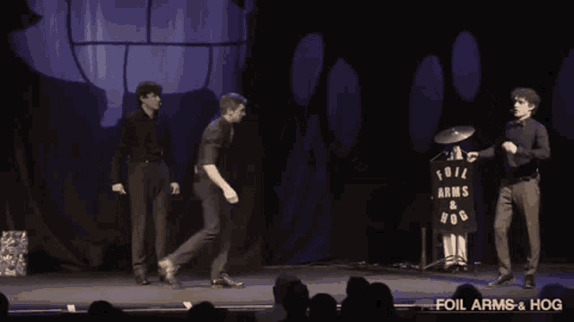 three men on a stage with a foil arms and hog sign