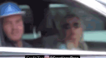 a man wearing a blue hard hat is driving a car next to a woman .