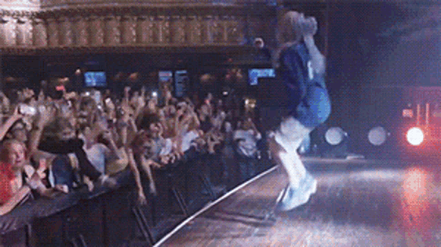 a woman in a blue hoodie is jumping on a stage