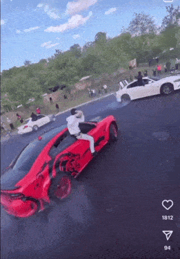 a man is sitting on the back of a red sports car