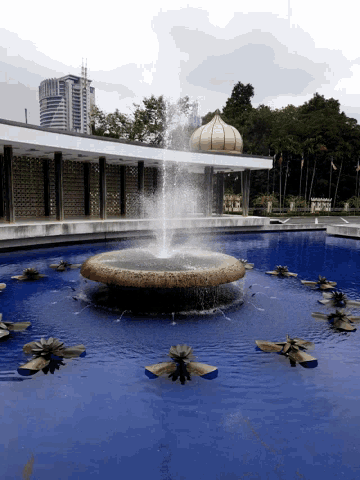 a fountain in a park with a building in the background that says ' sdn ' on it
