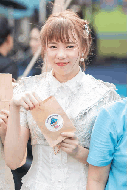 a girl in a white dress is holding a brown bag with a sticker on it that says ' bangkok ' on it
