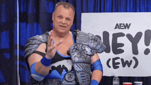 a wrestler stands in front of a sign that says aew on it