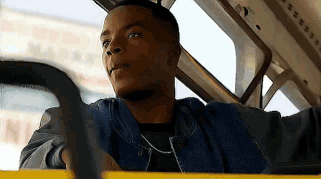 a young man is sitting in the driver 's seat of a bus looking out the window .