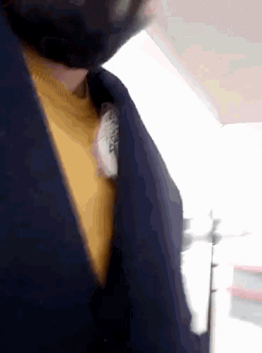 a man wearing a yellow sweater and a black jacket has a piece of paper sticking out of his jacket collar