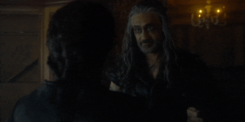a man with long hair and a beard is standing next to a woman in a dark room .