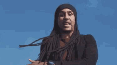 a man with dreadlocks is wearing a black hat and a watch while standing in front of a blue sky .
