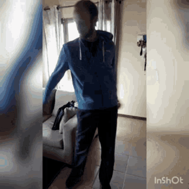 a man in a blue jacket is standing in front of a couch