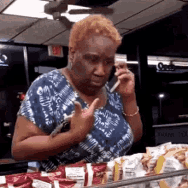 a woman is talking on a cell phone while standing in front of a display case of food .