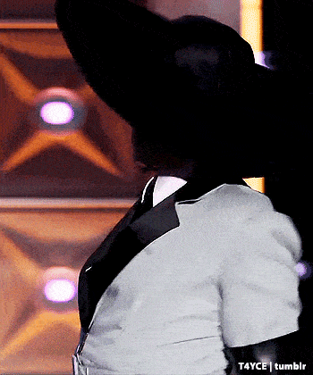a woman wearing a black hat and a white shirt is standing in a dark room .