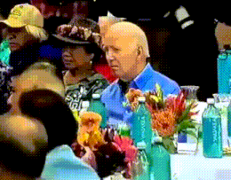 a man in a blue shirt sits at a table with flowers and water bottles that say aquafina
