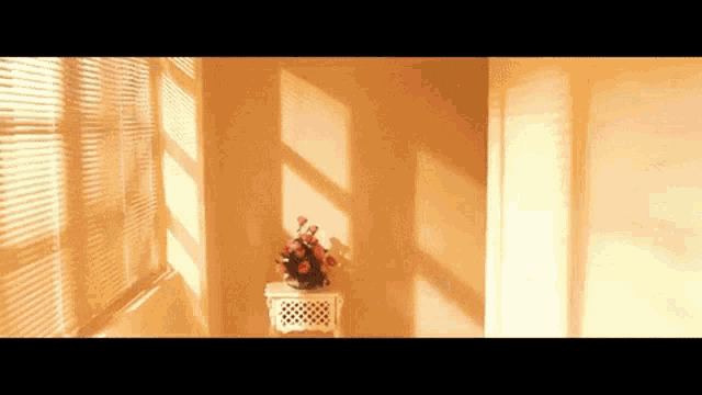 a vase of flowers sits on a small table in front of a window with blinds