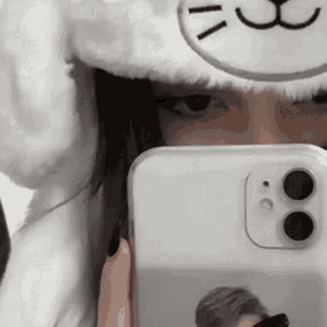 a woman is taking a selfie with her phone while wearing a cat hat .