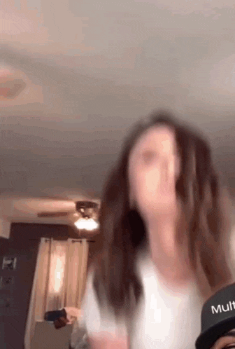 a woman wearing a white shirt and a black hat with the word mult on it is dancing in a living room .