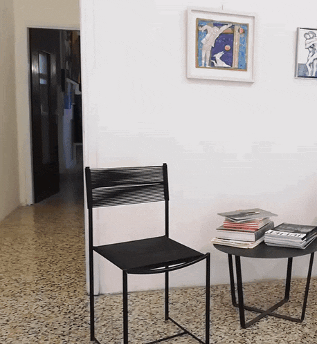 a black chair sits next to a table with books on it and a picture on the wall above it