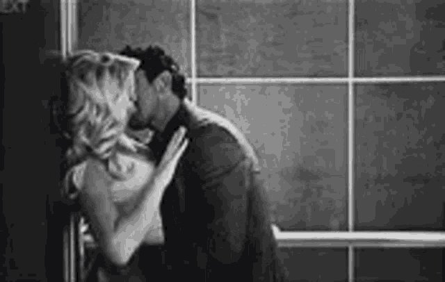 a man and a woman are kissing in front of a window in a black and white photo .