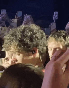 a man with curly hair is standing in front of a crowd of people taking pictures of him .