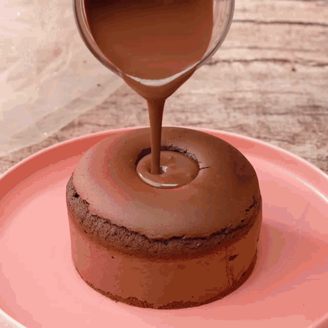 a chocolate cake is being poured with chocolate sauce on a pink plate