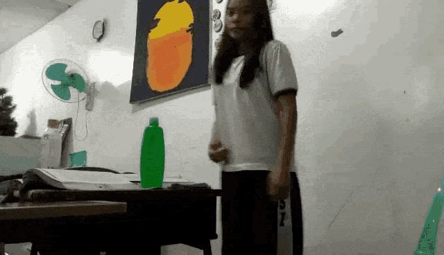 a girl standing in front of a table with a green bottle on it .
