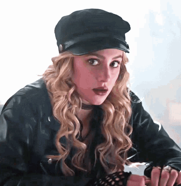 a woman wearing a black hat and a leather jacket looks at the camera