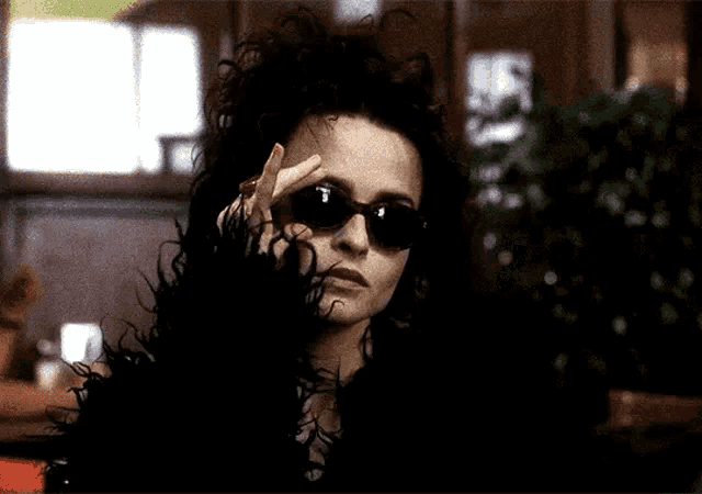 a woman wearing sunglasses and a fur coat is making a peace sign .