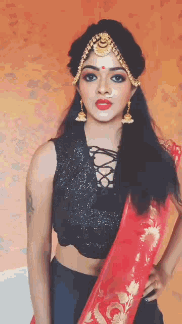 a woman wearing a black top and a red saree is posing for a picture .