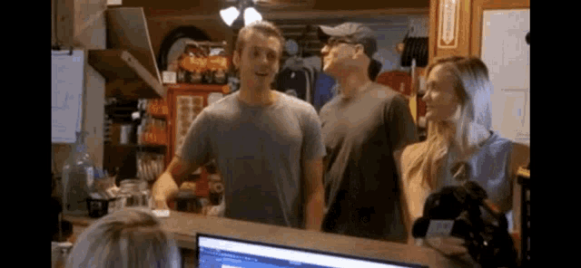 a group of people are standing around a counter in front of a computer monitor .