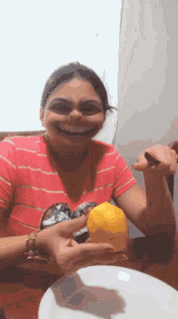 a woman in a pink striped shirt is smiling and holding a lemon